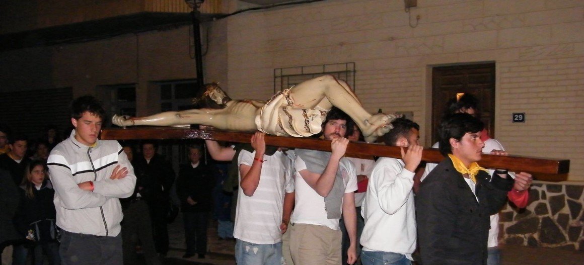Un grupo de jóvenes lleva a hombros una imagen de Cristo crucificado en una procesión nocturna de Semana Santa