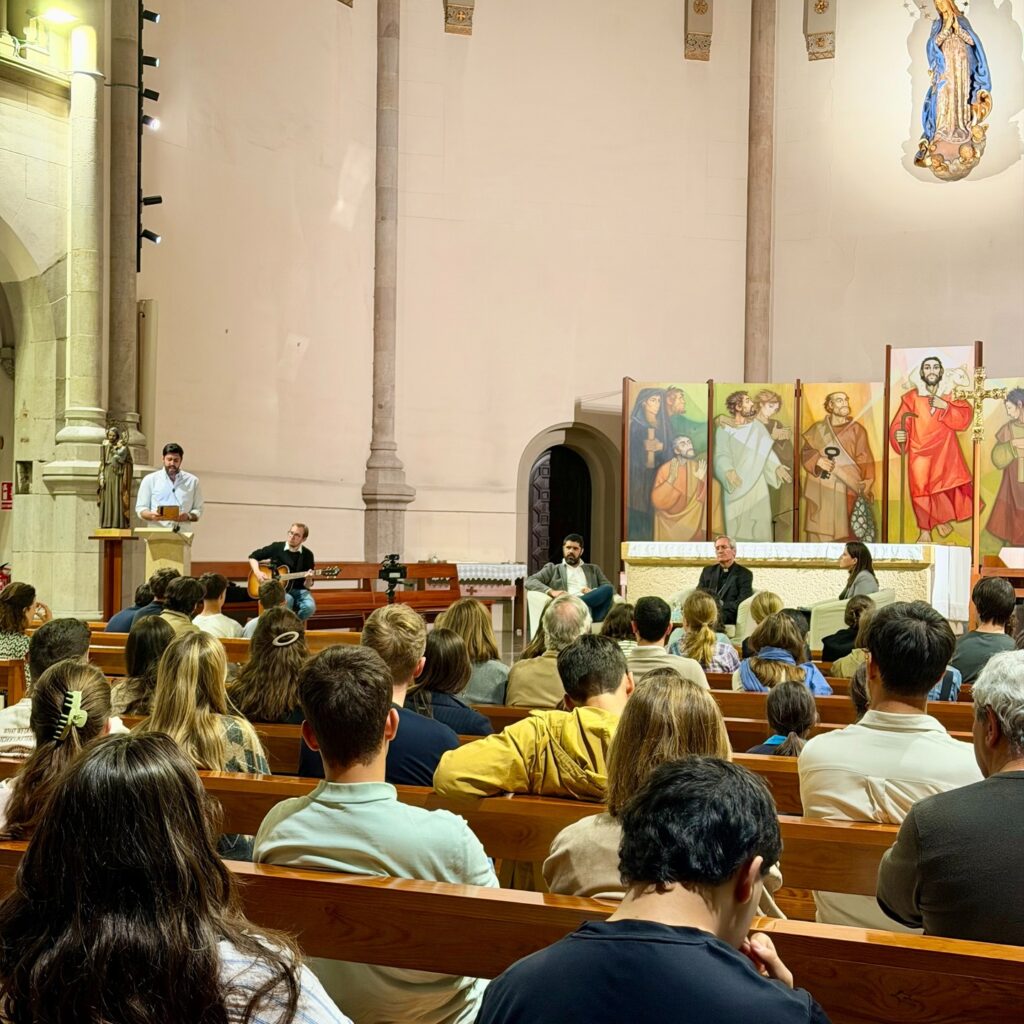 Audience seated in the pews while a guitarist accompanies the event beside the presbytery