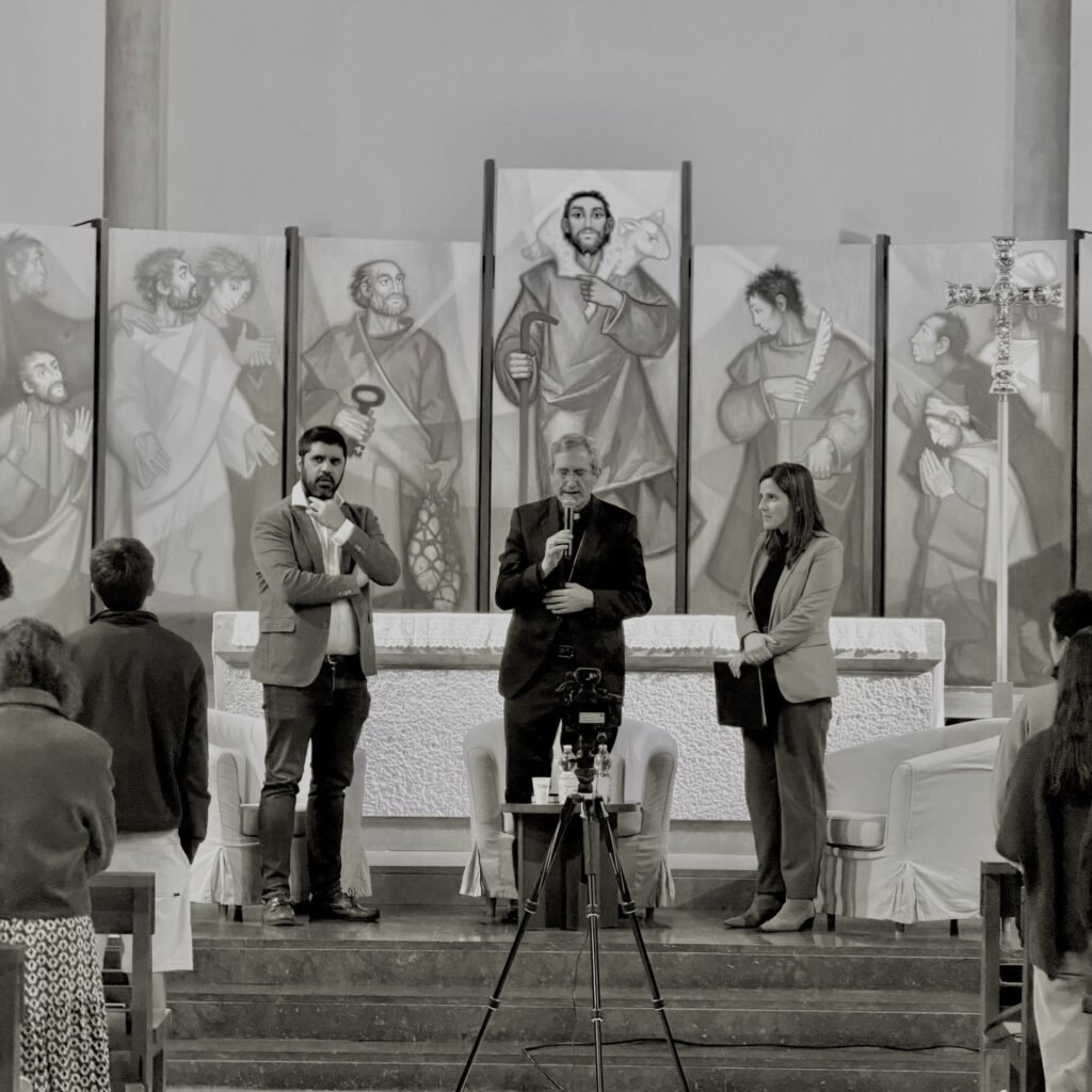 Black and white photograph of the two speakers and the moderator standing before the altar at the end of the event
