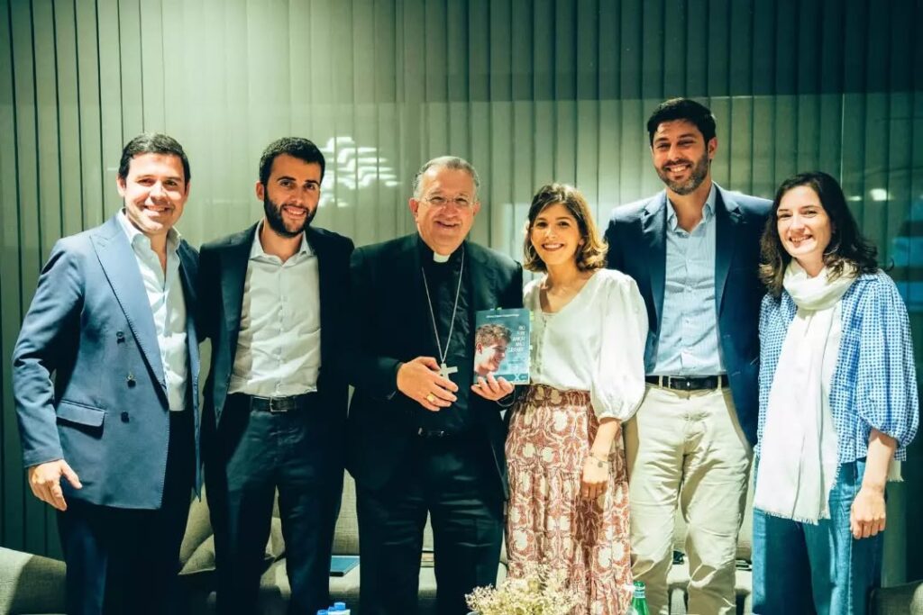Sei persone posano in piedi accanto a un divano; una di loro, un vescovo, tiene in mano una copia del libro.