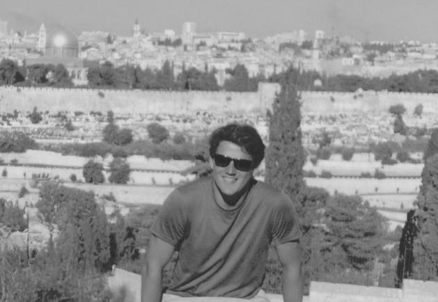 Marcos sorri, sentado no monte das Oliveiras, com a cidade velha de Jerusalém ao fundo