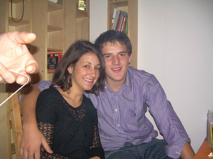Marcos Pou, con camisa de rayas, sonríe abrazado a una joven en una habitación con estanterías de madera