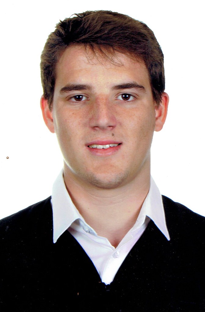 Retrato de carné de Marcos Pou sonriendo, con camisa blanca y jersey negro sobre fondo blanco