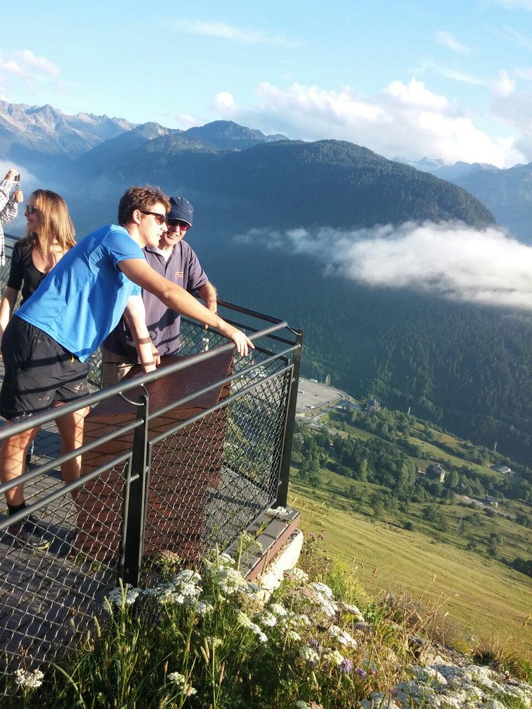 Marcos Pou apoyado en la barandilla de un mirador de montaña, junto a otros jóvenes, con valles y un mar de nubes al fondo