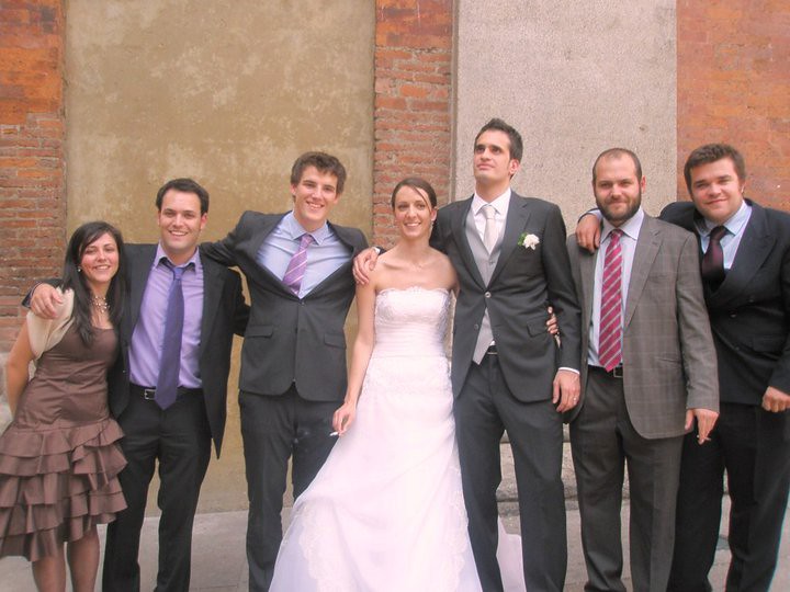 Los novios posan con un grupo de jóvenes vestidos de fiesta ante un muro de piedra y ladrillo el día de la boda