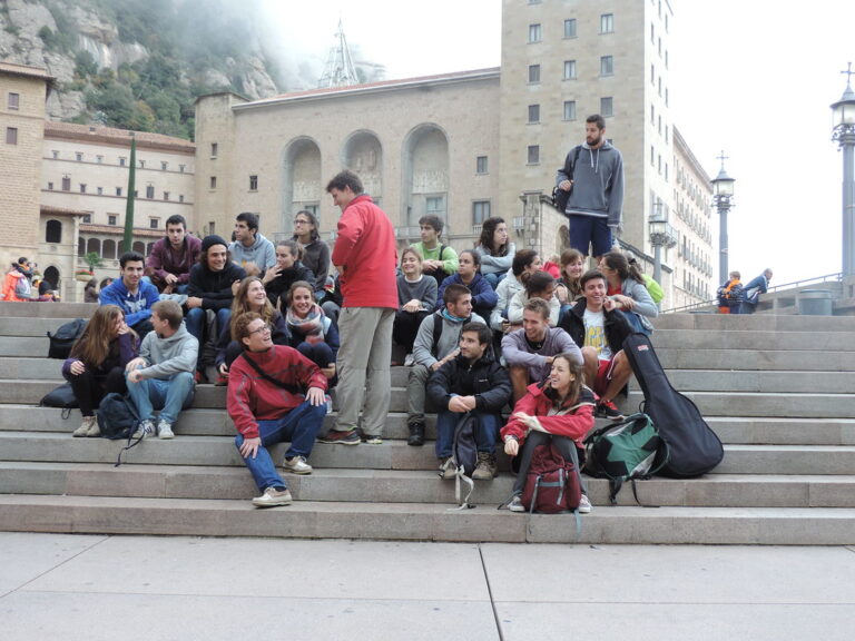 Grupo de jóvenes con mochilas y una guitarra sentados en las escaleras del monasterio de Montserrat