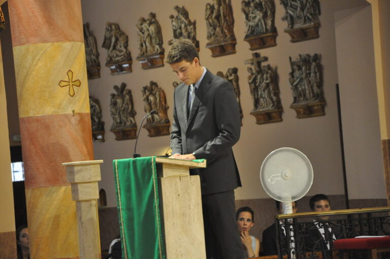 Marcos Pou, con traje gris, lee desde el ambón de una iglesia ante los asistentes