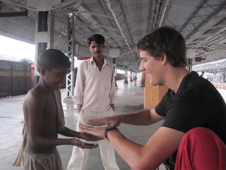 Marcos Pou sonriendo mientras juega con las manos con un niño en el andén de una estación, junto a un hombre que los observa