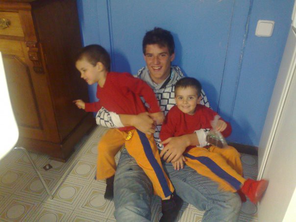 Marcos Pou sentado en el suelo de una cocina, sonriendo con dos niños pequeños vestidos de rojo en su regazo