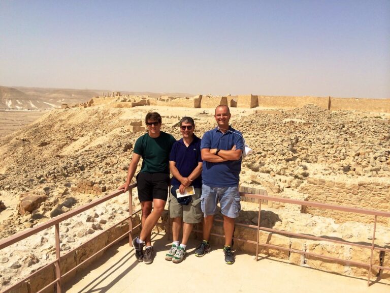 Marcos Pou junto a dos hombres posando en un mirador ante unas ruinas en pleno desierto