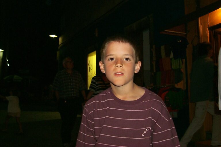 Marcos Pou de niño, con camiseta de rayas, en una calle de noche junto a escaparates y transeúntes