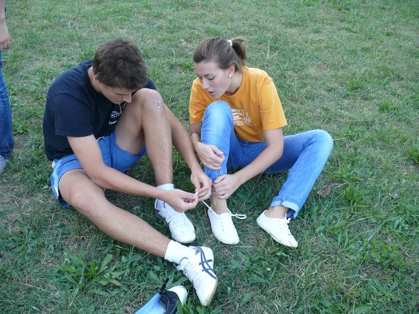 Un chico y una chica sentados sobre la hierba en el campo, atándose los cordones de las zapatillas