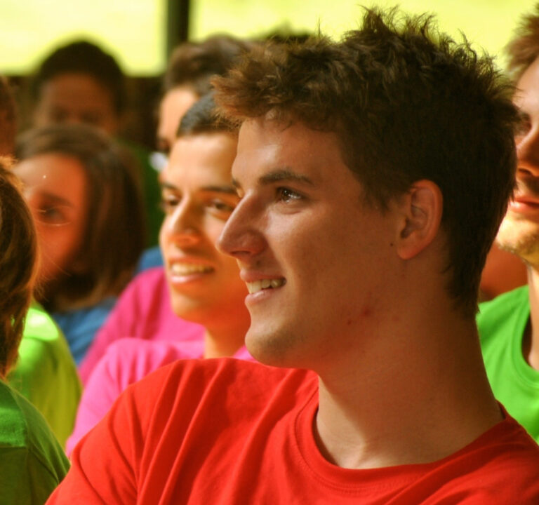 Marcos Pou, con camiseta roja, sonríe de perfil rodeado de un grupo de jóvenes con camisetas de colores
