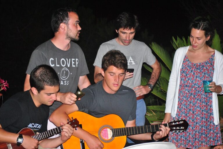 Grupo de jóvenes cantando de noche al aire libre, dos de ellos tocando la guitarra