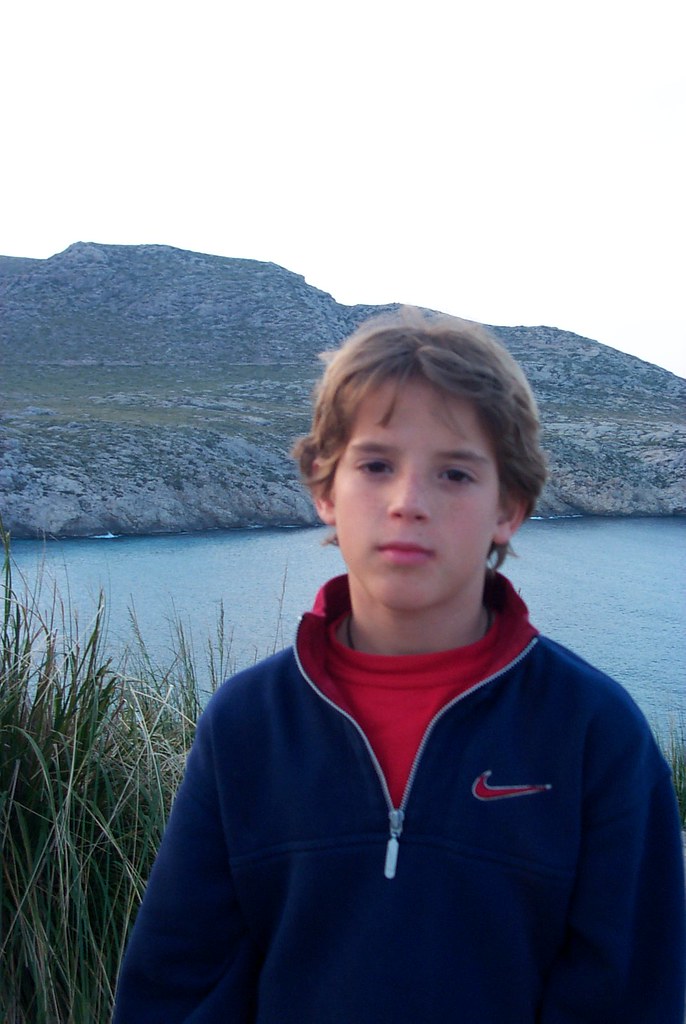 Marcos Pou as a child, wearing a blue fleece, posing before a cove surrounded by rocky mountains