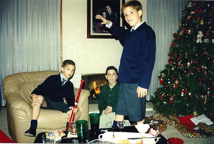 Tres niños posan en el salón de casa junto a la chimenea encendida y el árbol de Navidad decorado