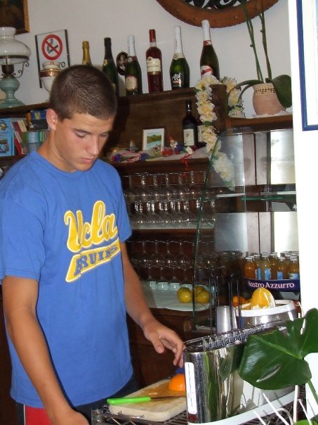 Marcos Pou, con camiseta azul de UCLA, exprimiendo naranjas tras la barra de un bar