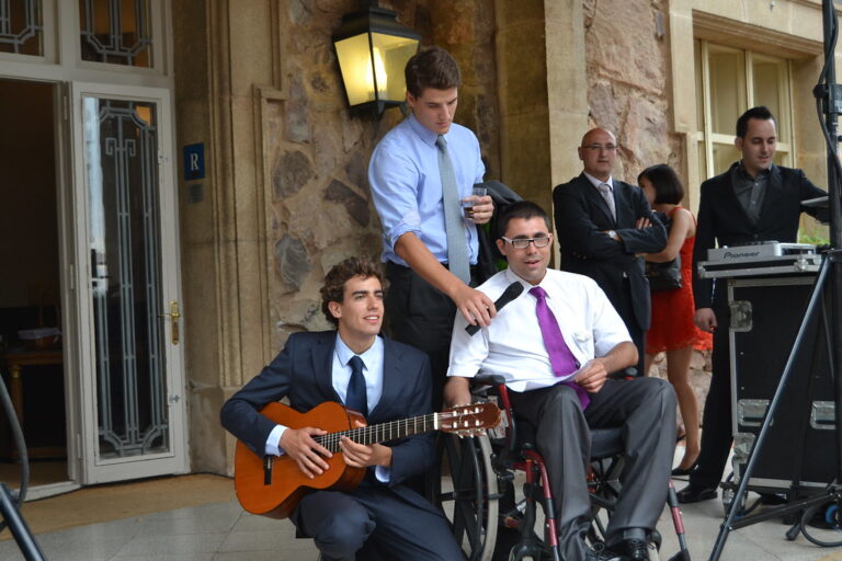 Un joven en silla de ruedas canta con un micrófono junto a otro joven que le acompaña con la guitarra en una celebración