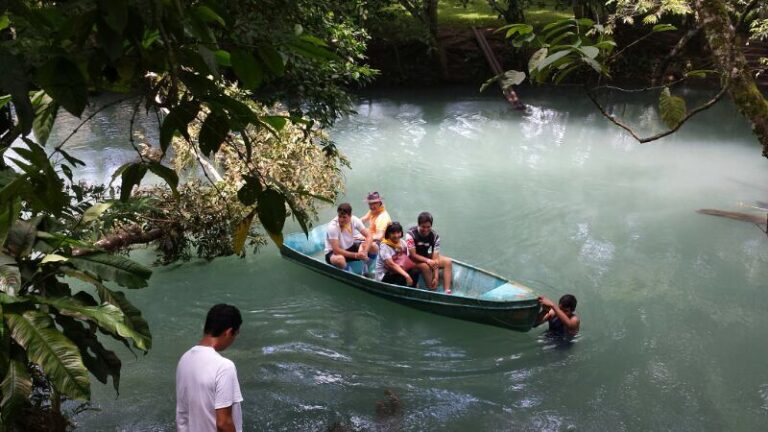 Grupo de jóvenes en una barca de madera sobre un río de aguas turquesas rodeado de vegetación tropical, mientras un niño empuja la embarcación