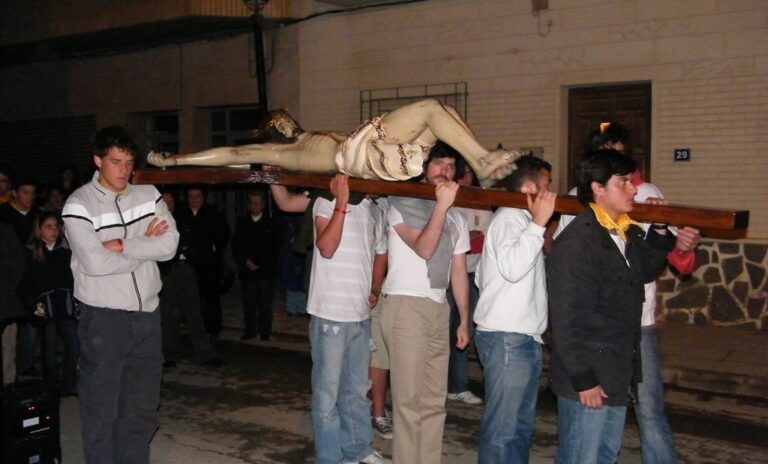 Un grupo de jóvenes lleva a hombros una cruz con la imagen de Cristo en una procesión nocturna por la calle