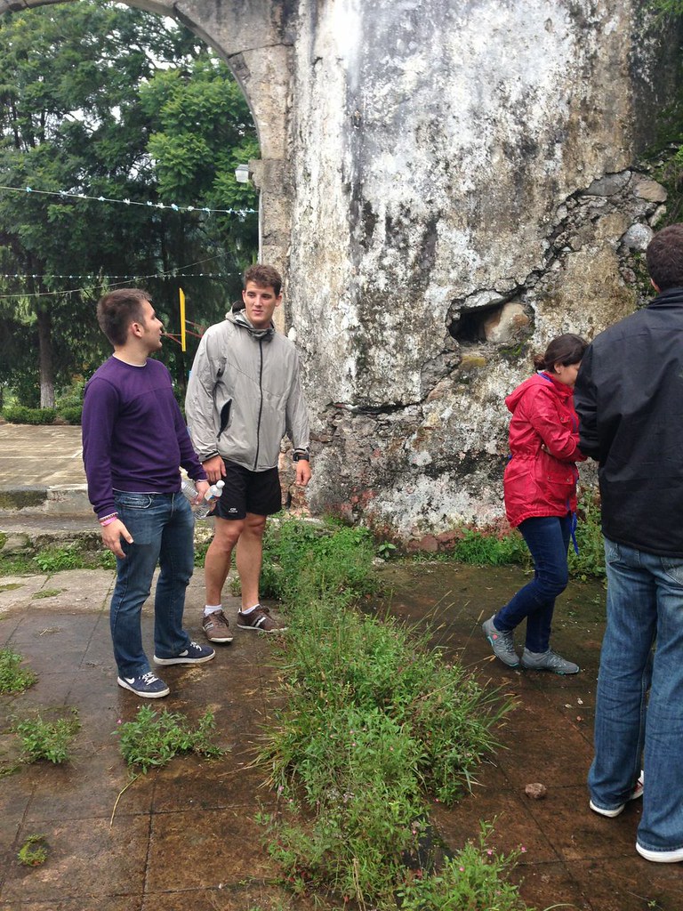 Marcos Pou conversando con unos jóvenes junto a un muro de piedra y un arco antiguo, al aire libre