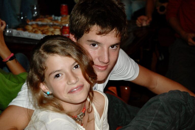 Marcos Pou, adolescente con camiseta blanca, posa sonriente junto a una niña en una reunión familiar con mesa de comida al fondo