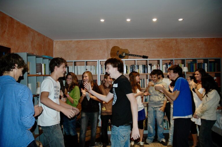 Grupo de jóvenes riendo y charlando de pie en una sala con estanterías de libros y una guitarra colgada en la pared