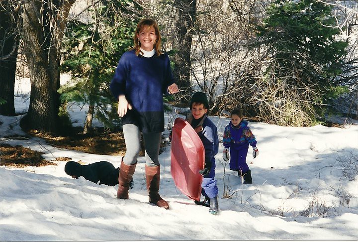 Una mujer y tres niños juegan en la nieve con un trineo rojo entre los árboles de un bosque