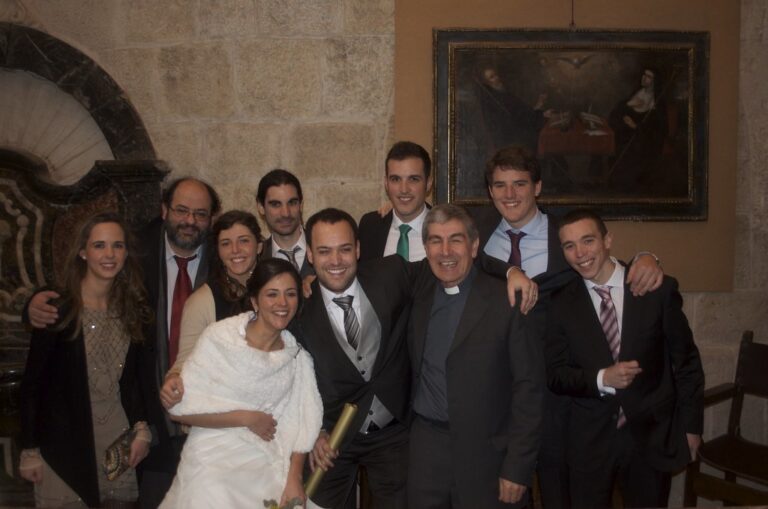 Los novios rodeados de familiares, amigos y un sacerdote posando sonrientes en el interior de una iglesia el día de la boda
