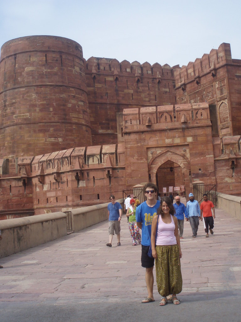 Marcos Pou, con gafas de sol y camiseta azul, posa junto a una joven ante la puerta del fuerte rojo de Agra, en la India