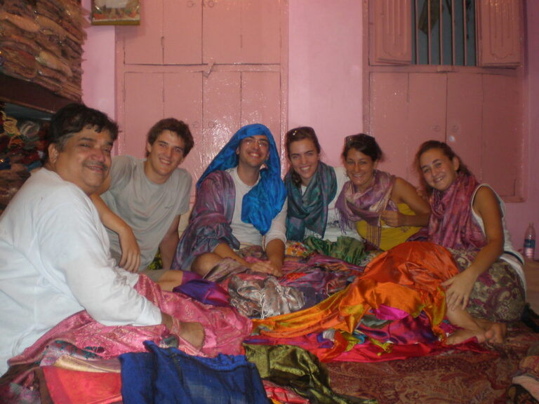 Grupo de jóvenes sentados en el suelo entre telas de colores en una tienda de tejidos, junto al vendedor, en un viaje