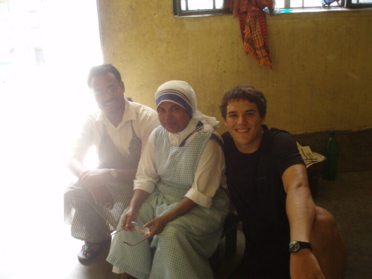Marcos Pou sonriente junto a una religiosa con hábito y un voluntario, sentados en una sala durante un viaje misionero