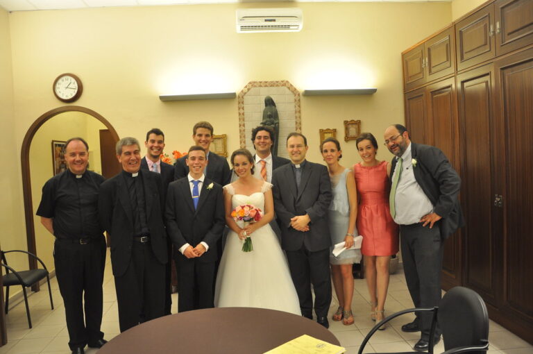 Los novios de una boda posando en la sacristía con familiares, amigos y tres sacerdotes tras la ceremonia