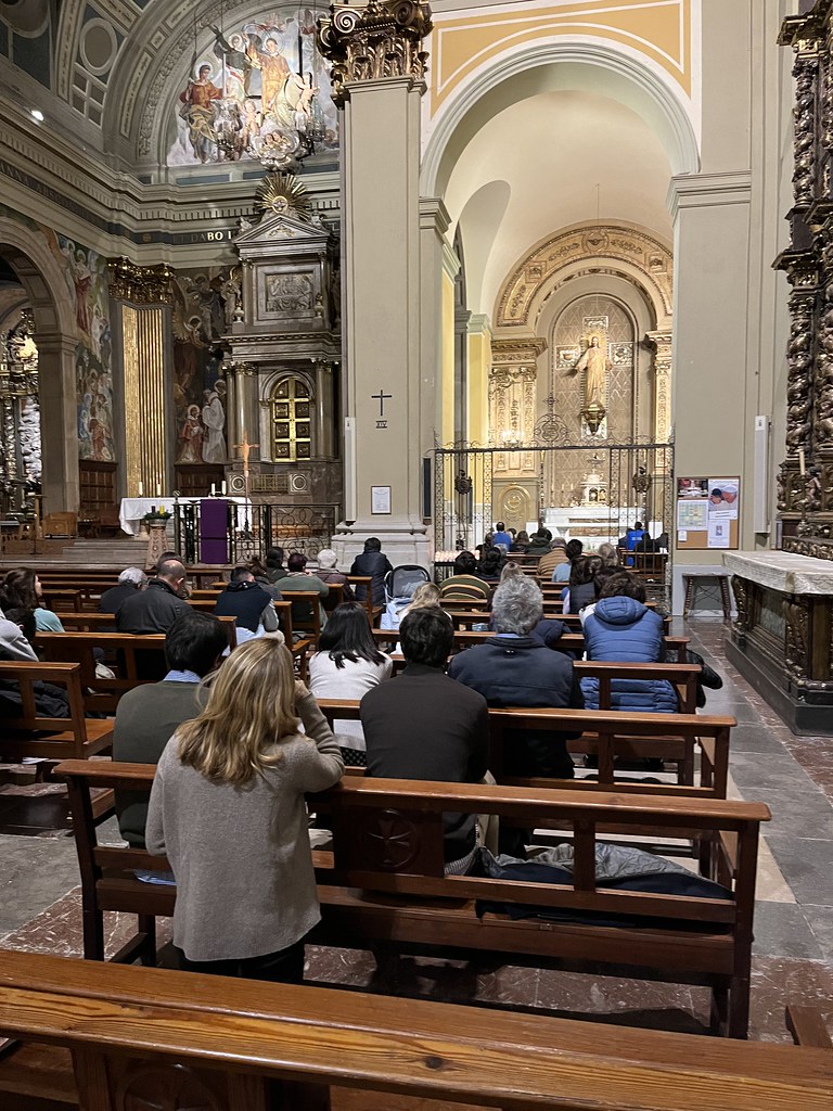 Fieles sentados en los bancos de una iglesia durante una celebración, con el altar y las capillas laterales al fondo