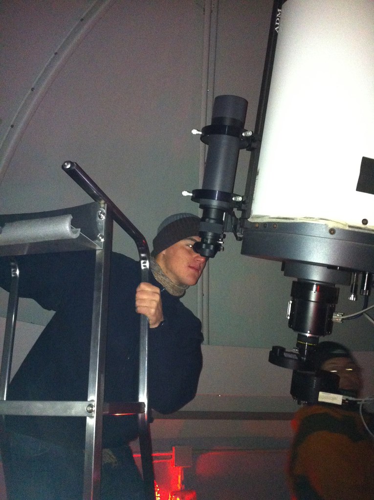 Marcos Pou, wearing a woollen hat, standing on a ladder and looking through the eyepiece of a large telescope in an observatory
