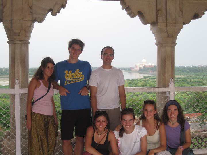Grupo de jóvenes posando bajo un templete de piedra con el Taj Mahal y el río al fondo durante un viaje a la India