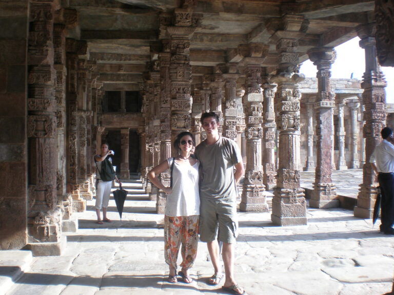 Marcos Pou posa junto a una joven entre las columnas talladas de un templo de piedra durante un viaje