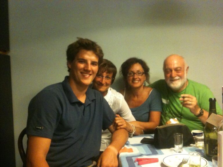 Marcos Pou sonriendo con polo azul sentado a la mesa junto a dos mujeres y un hombre durante una comida familiar