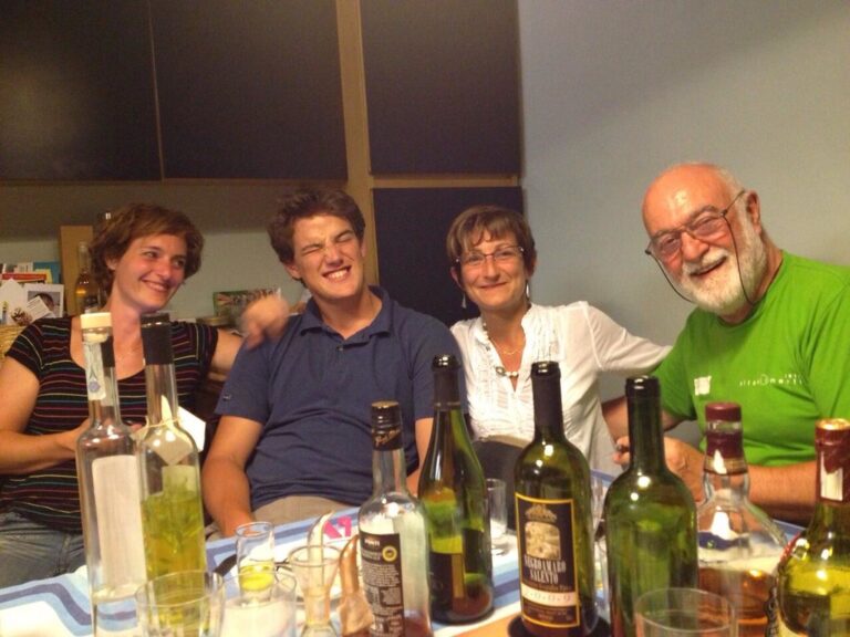 Marcos Pou sonriendo junto a dos mujeres y un hombre mayor sentados a una mesa con botellas y vasos durante una cena