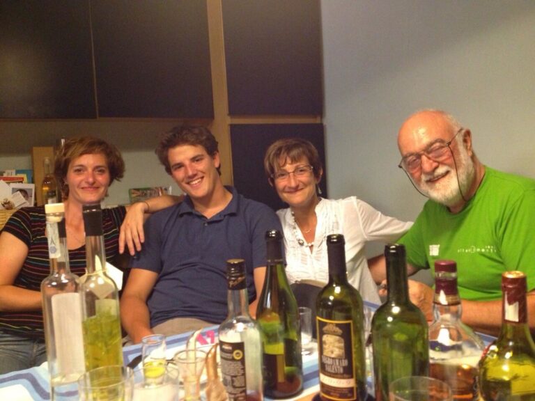 Marcos Pou sonriendo junto a dos mujeres y un hombre mayor alrededor de una mesa con botellas y vasos durante una comida
