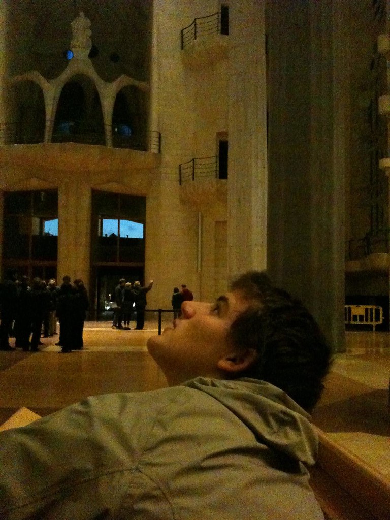 Marcos Pou recostado con la cabeza hacia atrás contemplando el interior de un gran templo con visitantes al fondo