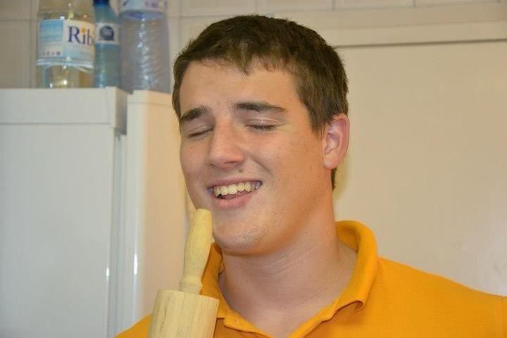 Marcos Pou, con polo naranja, sonríe con los ojos cerrados en una cocina mientras sostiene un rodillo de madera